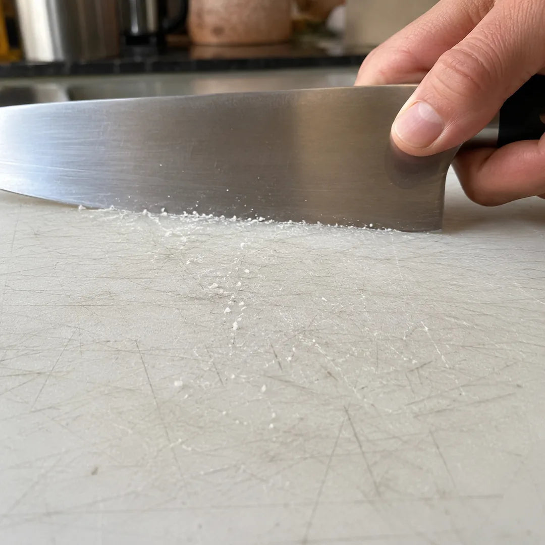 Un couteau entaille une planche en plastique blanche déjà rayée